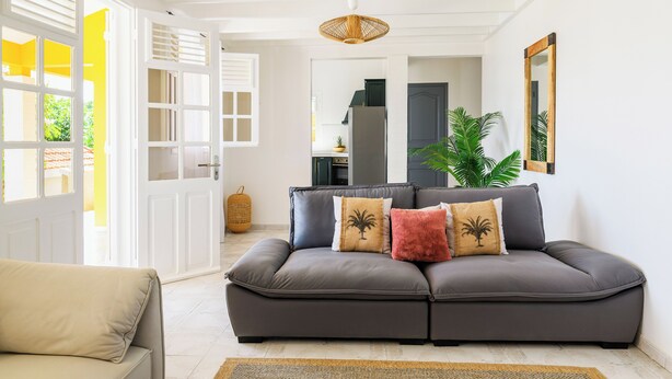 A living room with a grey sofa, a beige armchair, and a large window with white shutters. - Villa Caryota | Mountain Panorama & 29ft (9m) Private Pool (le Marin)