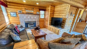 Acogedor interior de cabaña de madera con chimenea, muebles de madera y televisor.
