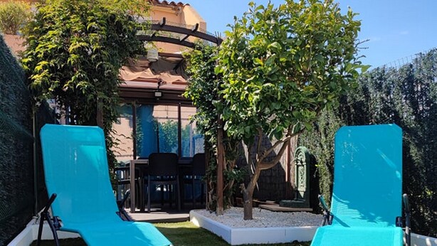 Two blue lawn chairs in a garden with a building in the background.