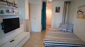 A bedroom with a bed, a TV on a stand, a door, and a hallway.