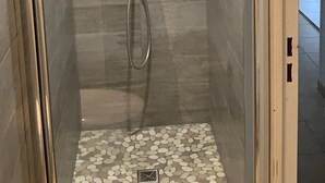 A walk-in shower with a glass door, tiled walls, and a pebble-patterned floor.