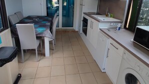A compact kitchen with a dining area, a washing machine, and a view through the glass door.
