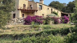 Un edificio de piedra con un balcón, rodeado de abundante vegetación y flores púrpuras.