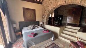 Un dormitorio con un arco de piedra, una cama con colcha estampada, un escritorio con silla y un aparador de madera.