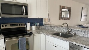 Een moderne keuken met witte kastjes, een roestvrijstalen fornuis, een magnetron, een spoelbak en een vaatwasser.