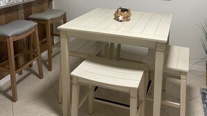 Een keuken met een wit aanrecht, houten krukken, een witte tafel en een bank.