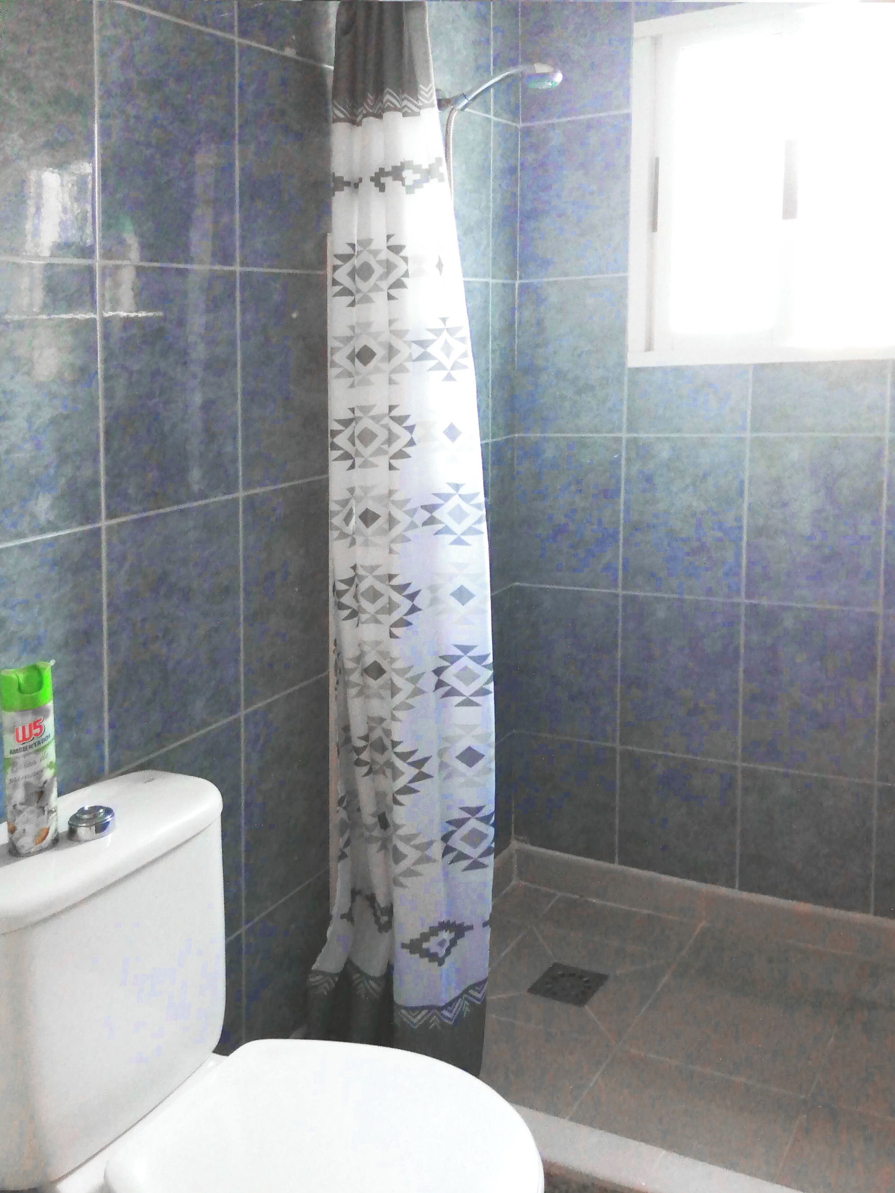 A bathroom with a toilet, a shower with a patterned curtain, and blue-tiled walls.