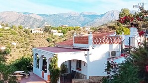 A white building with a red-tiled roof and arched windows, surrounded by greenery and mountains in the background. - Andalusian finca with private pool, sea views and stunning sunsets (Torrox)