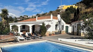 A swimming pool with lounge chairs, a white building with arches, and a hillside backdrop. - Andalusian finca with private pool, sea views and stunning sunsets (Torrox)