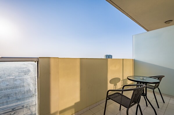 Un balcón con una mesa y sillas de vidrio, vista al cielo y un edificio al fondo.
