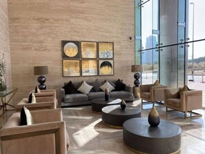 A modern lobby with a large window, a grey sofa, and a coffee table. - Elegant 2BR in Tower 108 Jumeirah Village Circle by Deluxe Holiday Homes (Dubai)
