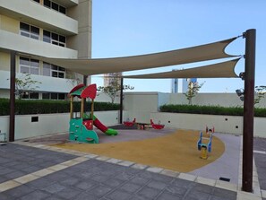 A children's play area with a slide, climbing structure, and swings, surrounded by a shaded canopy. - Elegant 2BR in Tower 108 Jumeirah Village Circle by Deluxe Holiday Homes (Dubai)