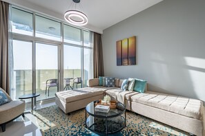 A modern living room with a sectional sofa, a glass coffee table, and a view of the city through large windows. - Elegant 2BR in Tower 108 Jumeirah Village Circle by Deluxe Holiday Homes (Dubai)