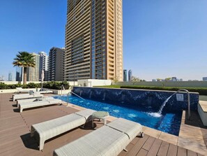 A rooftop pool area with lounge chairs, a small hot tub, and a view of surrounding high-rise buildings. - Elegant 2BR in Tower 108 Jumeirah Village Circle by Deluxe Holiday Homes (Dubai)