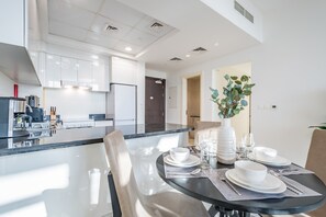 A modern kitchen with white cabinets, a dining area with a glass table, and a plant. - Elegant 2BR in Tower 108 Jumeirah Village Circle by Deluxe Holiday Homes (Dubai)