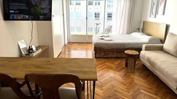 A hotel room with a bed, a sofa, a TV, a wooden table, and a chair. - Bright Apartment with Terrace to Faculties (Buenos Aires)