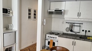 A compact kitchen with white cabinets, a gas stove, a microwave, and a coffee maker. - Bright Apartment with Terrace to Faculties (Buenos Aires)