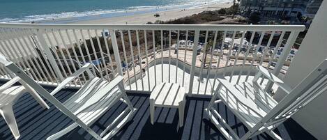 A balcony with white chairs overlooking a beach and a high-rise building.