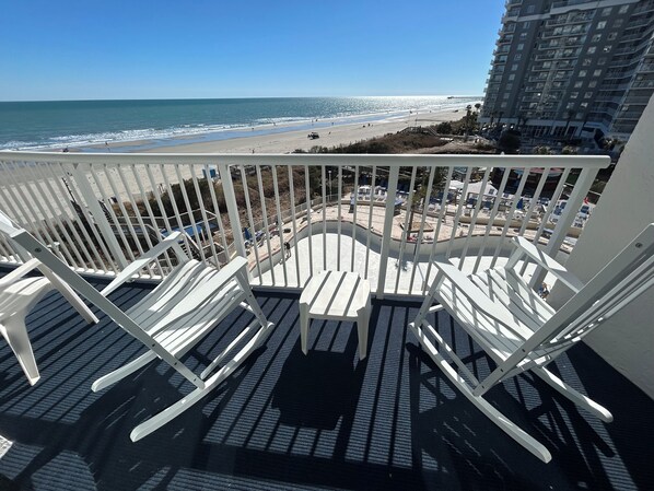A balcony with white chairs overlooking a beach and a high-rise building. - Seawatch Resort (Myrtle Beach)
