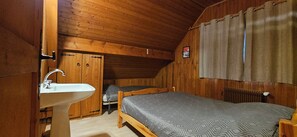 Une chambre dans une cabane en bois, avec un lit, une armoire en bois et un lavabo.