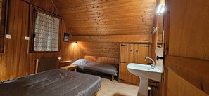 Une chambre dans un chalet en bois, avec deux lits, une armoire en bois, un radiateur et un lavabo.