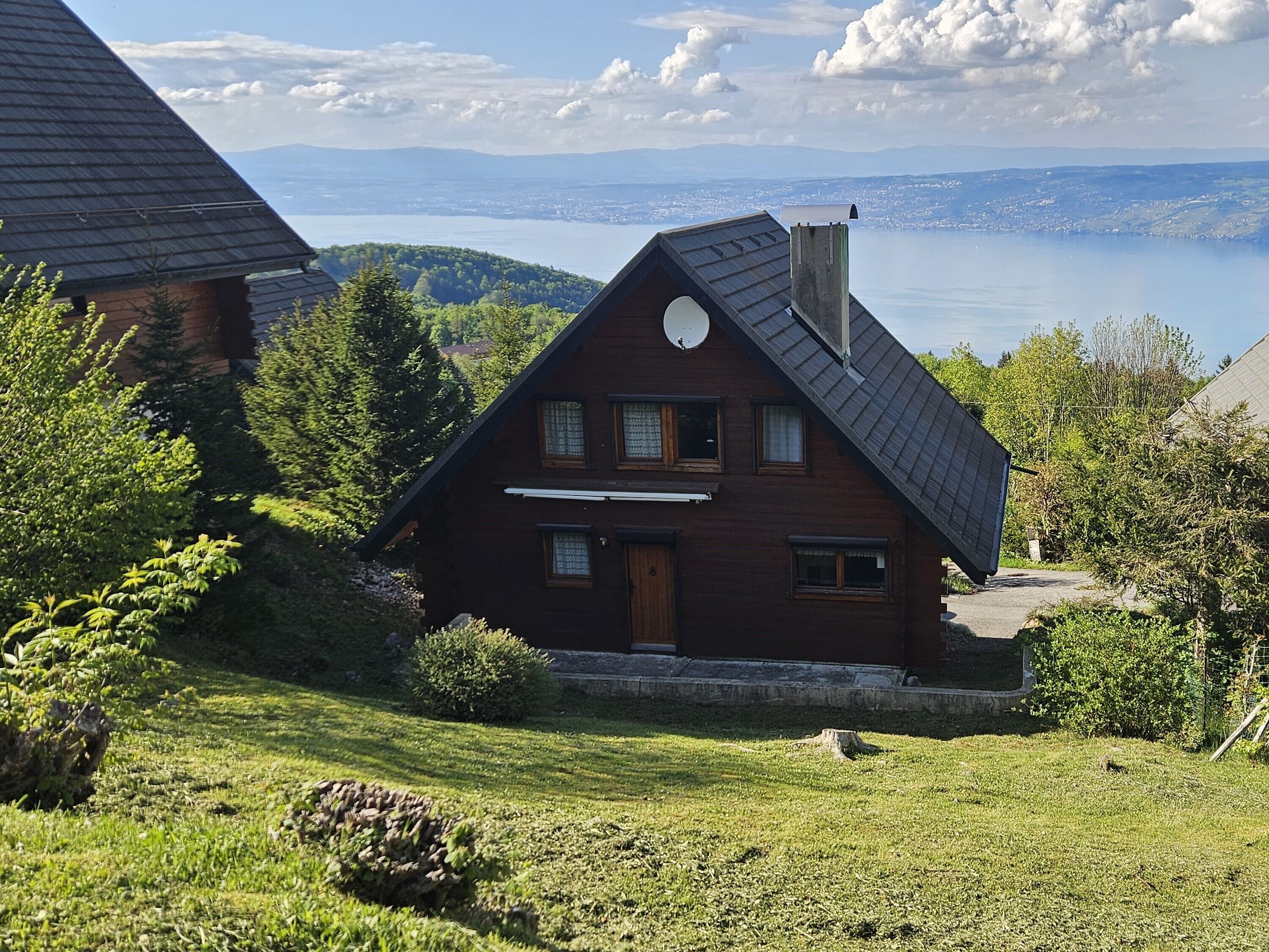 Une maison en bois avec un toit en pente, une antenne parabolique et une vue sur un lac et des montagnes en arrière-plan.