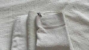 Une serviette blanche, soigneusement pliée, est posée sur un couvre-lit blanc à texture.
