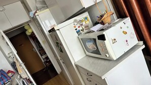 Une cuisine compacte équipée d’un four à micro-ondes, d’un petit réfrigérateur et d’un évier. On y trouve divers ustensiles de cuisine et un panier posé sur le plan de travail.