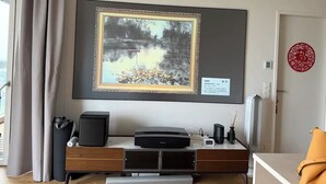 Une pièce avec un grand tableau encadré représentant un paysage, un meuble de divertissement moderne doté de haut-parleurs et un objet décoratif rouge accroché au mur.