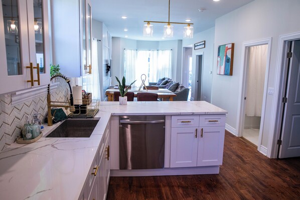 Una cocina moderna con armarios blancos, lavavajillas y un comedor con sofá y mesa.