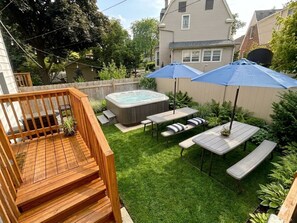 Patio trasero con hidromasaje, terraza de madera y mesas de picnic bajo sombrillas azules.