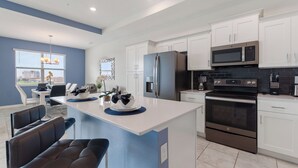 A modern kitchen with white cabinets, stainless steel appliances, and a blue accent wall. - South View Balcony Overlooking Water Sleeps 6 (Kissimmee)