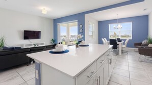 A modern kitchen with a white island, a dining area with a table and chairs, and a living area with a sofa and TV. - South View Balcony Overlooking Water Sleeps 6 (Kissimmee)