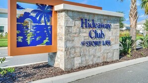 A sign for Hideaway Club at Storey Lake, featuring a stone wall and a decorative blue mural with palm trees and water. - South View Balcony Overlooking Water Sleeps 6 (Kissimmee)