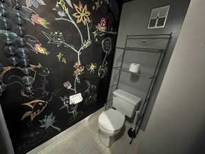 A bathroom with a toilet, a shelf, and a wall with floral and bird patterns. - Downtown Cabin | Pet Friendly | Walk to Everything (Tallahassee)