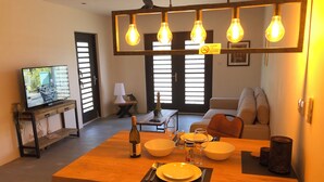 Un comedor con una mesa de madera dispuesta para dos personas, una botella de vino y un televisor al fondo.