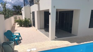 Un área de piscina con piscina azul, dos sillas azules y una mesa con sillas.