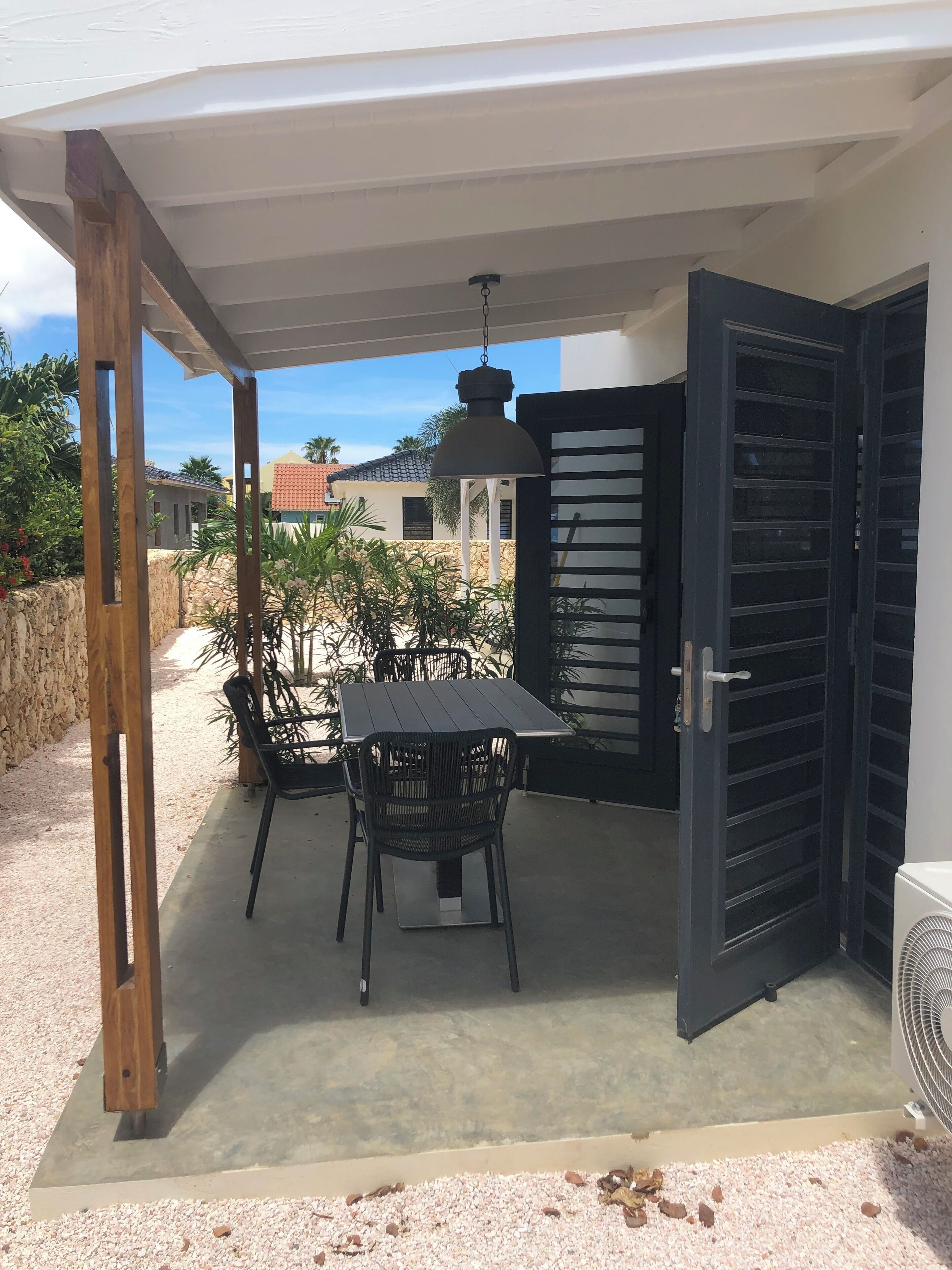 A covered patio area with a table and chairs, a black door, and a fan.