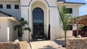 Un edificio moderno con una amplia entrada en arco, un patio con sillas y un muro de piedra.