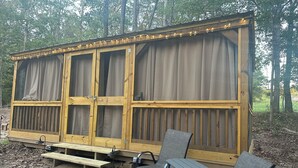 A wooden structure with large windows and curtains, a bench, and two chairs.