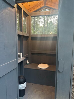 En lille, lukket trækonstruktion med toilet, skraldespand og en hylde med toiletpapir.