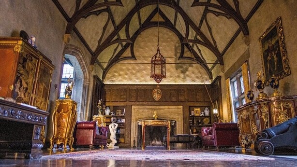 Une vaste pièce dotée d’un plafond haut, de poutres en bois décorées, d’un lustre et d’une cheminée.