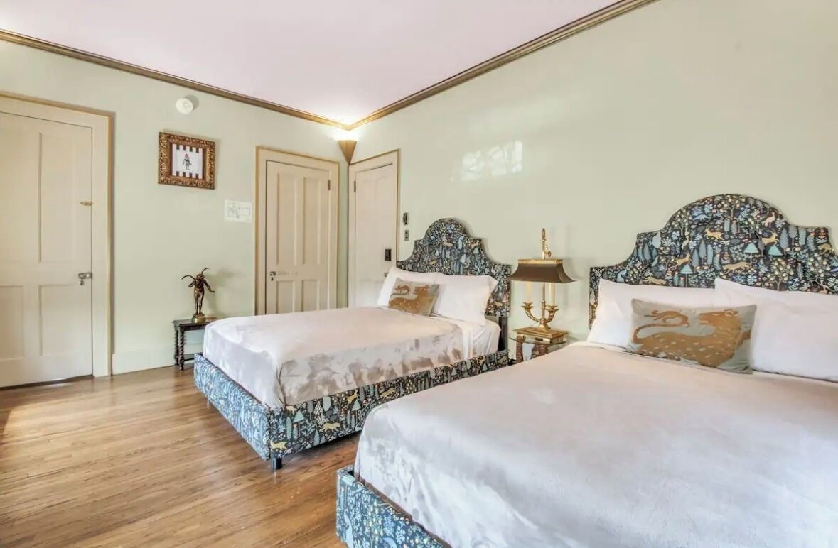 A bedroom with two beds, a nightstand, and a wall-mounted lamp.