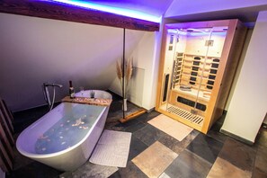 Ein modernes Badezimmer mit einer freistehenden Badewanne, einer Holzauna und einem großen Spiegel.