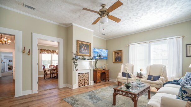 A spacious living room with hardwood floors, a ceiling fan, a fireplace, and a dining area visible through an open doorway.