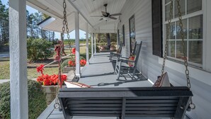 A porch with a swing, a ceiling fan, and a window with a chain hanging from it.