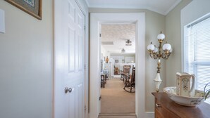 A hallway leading to a dining area with a chandelier, a wooden dresser, and a window with blinds.