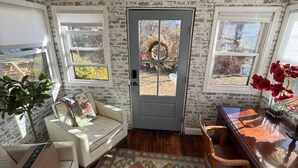 A room with a wooden ceiling, a gray door, a patterned rug, a white sofa, a wooden table, and a potted plant. - The Sun Filled Cozy Creamery (Plainville)