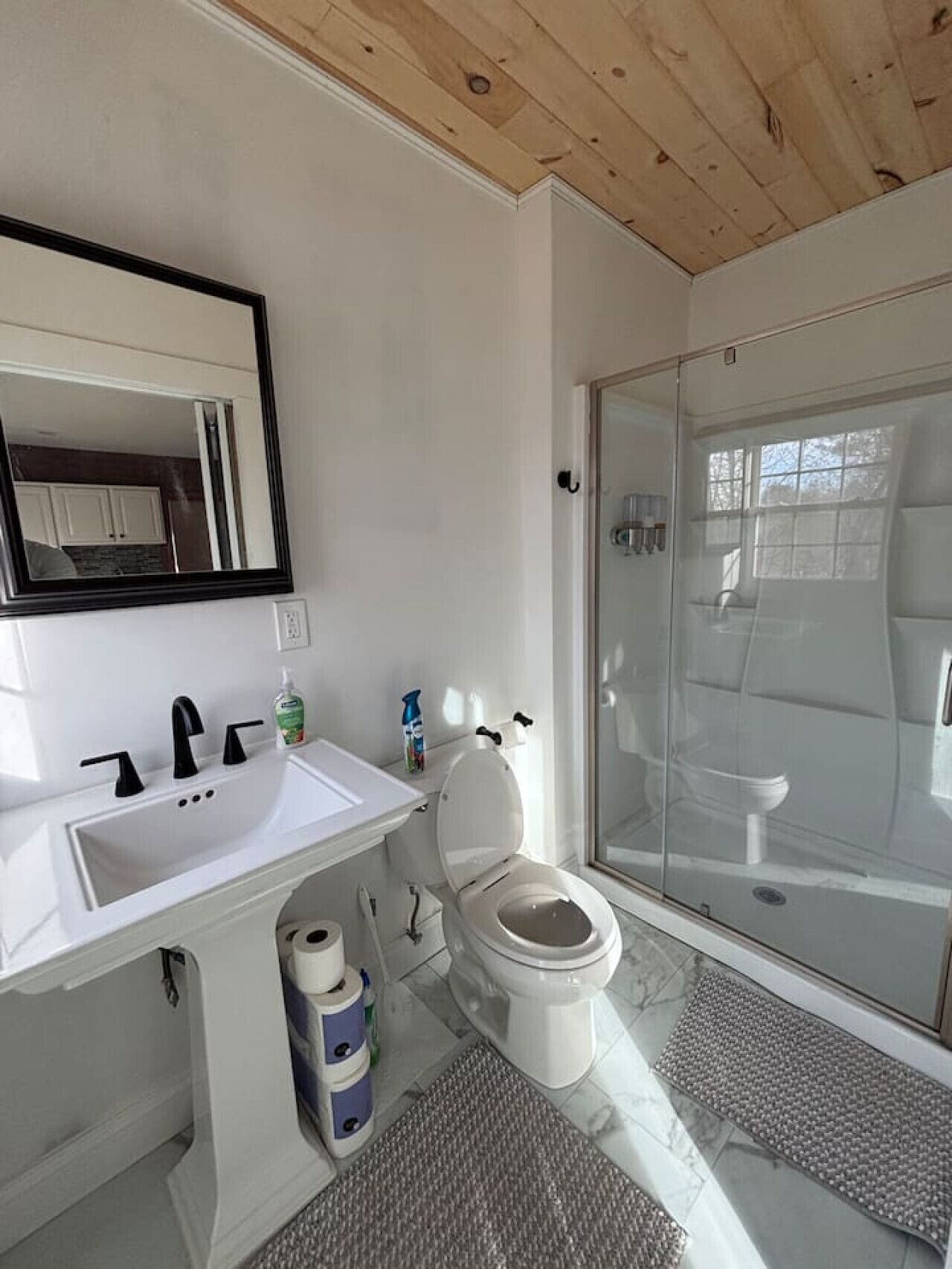 Une salle de bain moderne avec un lavabo blanc, des robinets noirs, des toilettes et une douche à parois de verre.