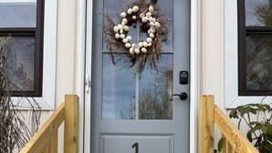 A wooden front door with a wreath, a number plaque, and a small porch with wooden railings. - The Sun Filled Cozy Creamery (Plainville)